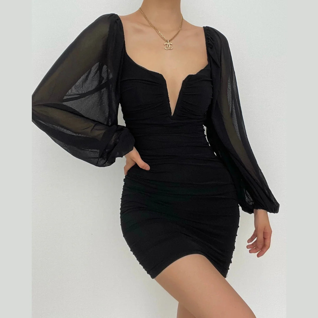 Woman wearing a black bodycon mini dress with sweetheart neckline and sheer long sleeves.