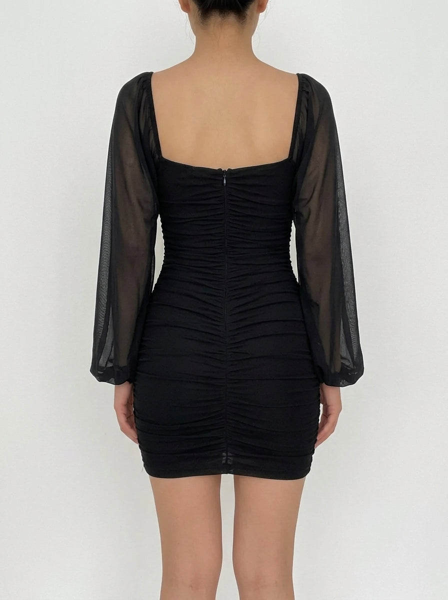 Side view of a woman in a black ruched bodycon mini dress with mesh sleeves.