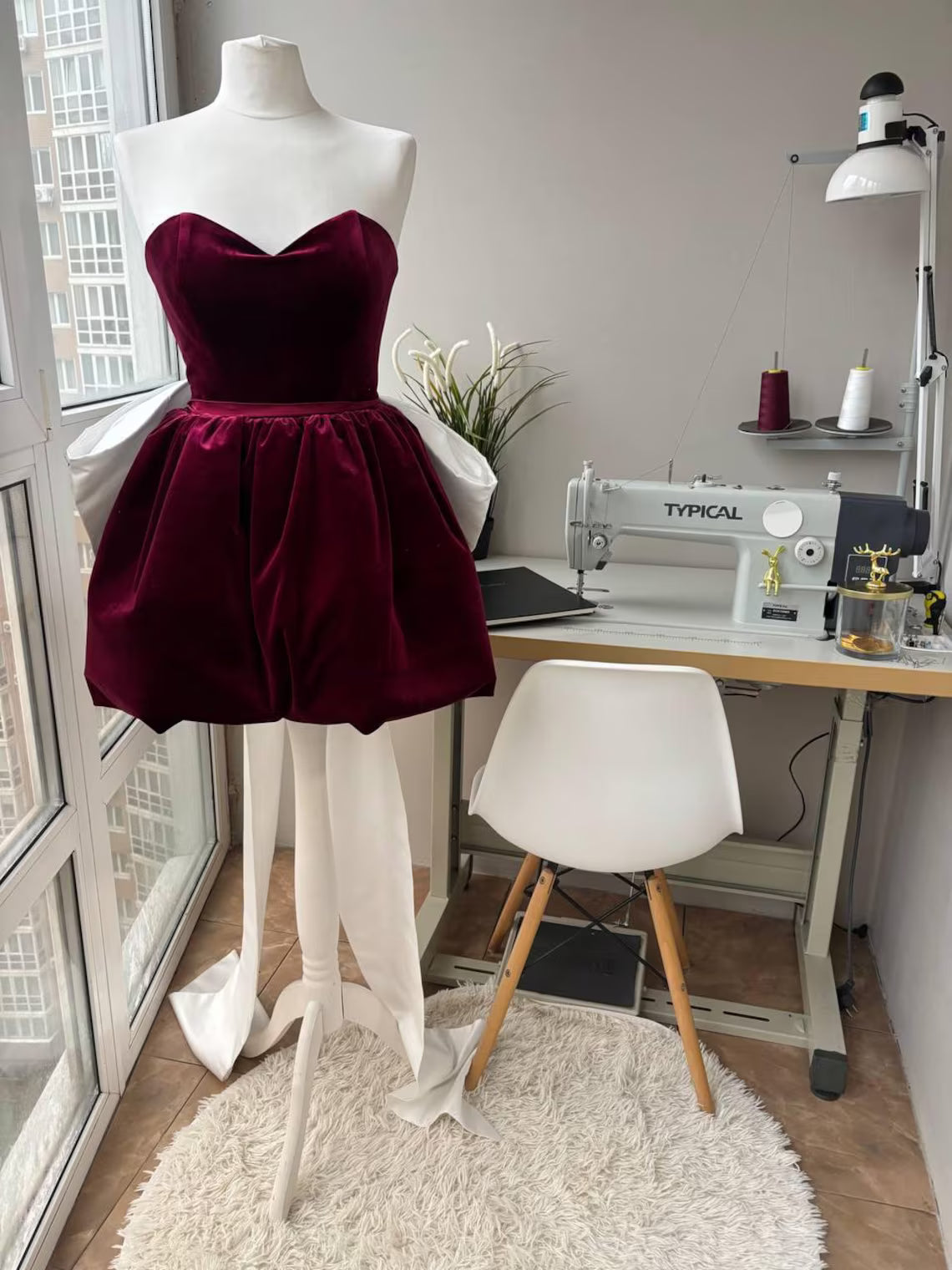 Model wearing a burgundy velvet A-line homecoming dress with a sweetheart neckline and dramatic white bow.