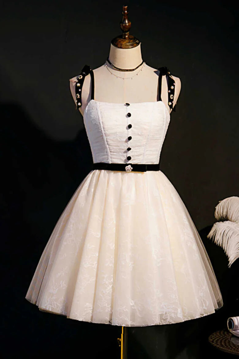 Front view of a model wearing a beige A-line homecoming dress with bow straps and black waist sash.