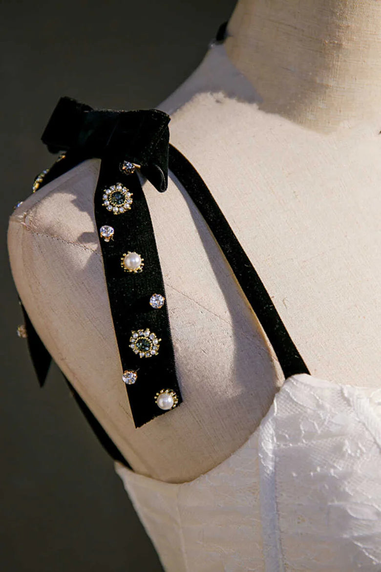 Side profile of the short beige A-line dress with bow straps and a black sash.