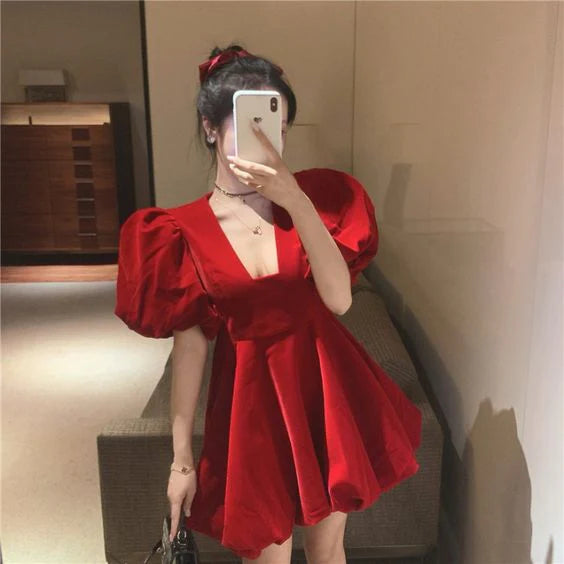 Front view of a red short homecoming dress with a low neckline and bubble sleeves.