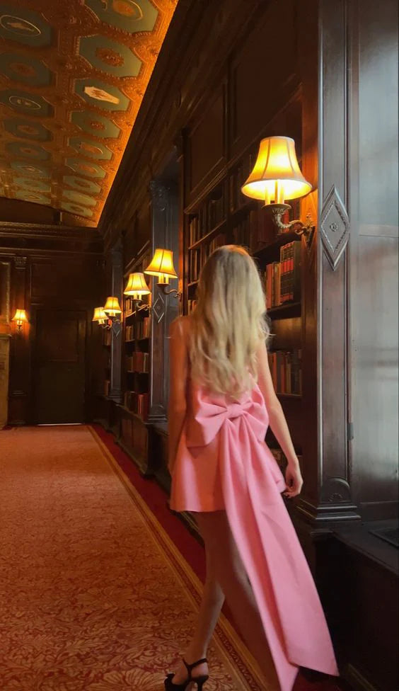 Side profile of a model in a pink satin short dress, emphasizing the fitted waist and flow of the skirt.