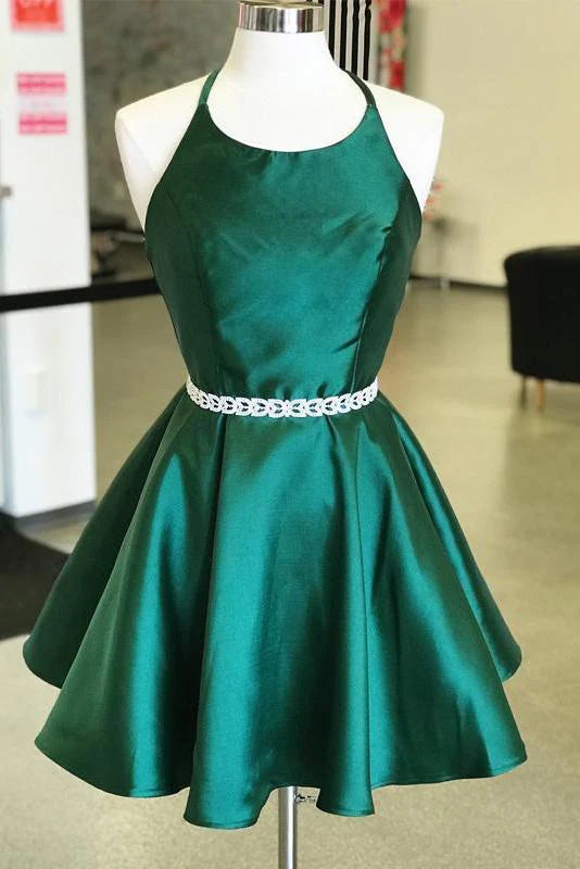 Woman wearing a dark green satin mini homecoming dress with an open back and halter neckline.