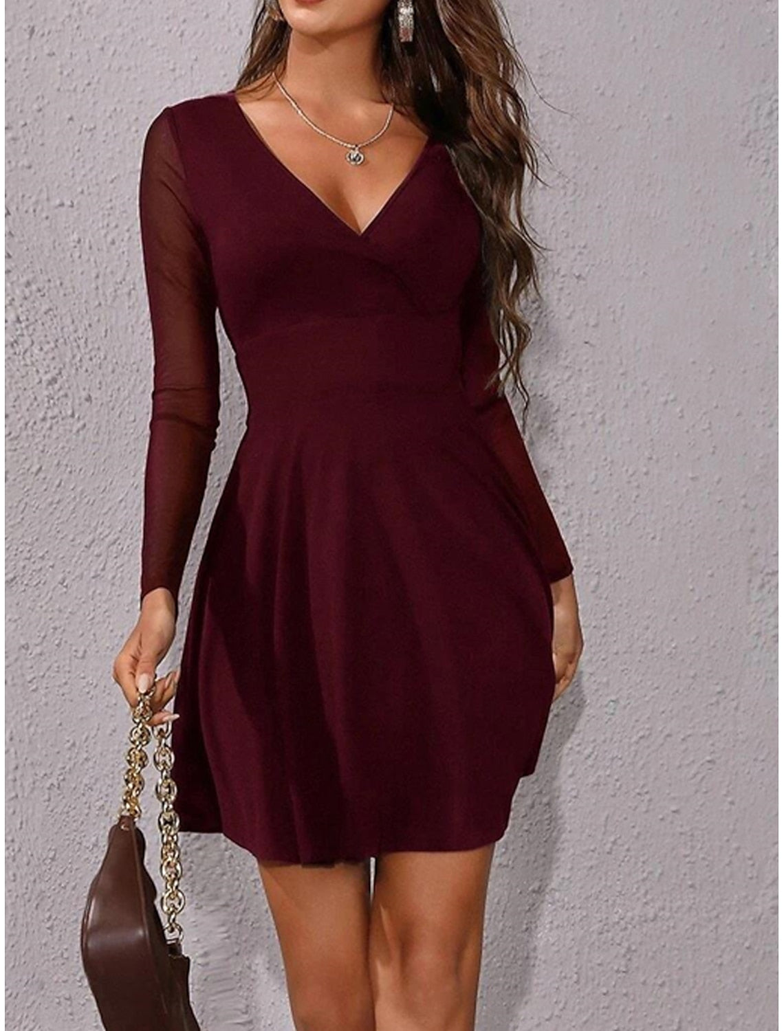 Woman wearing a black ruched mesh V-neck long sleeve mini dress, front view.