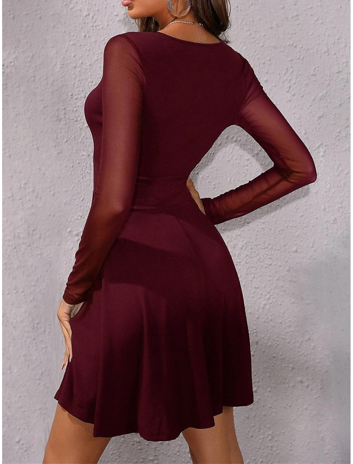 Woman wearing a black ruched mesh V-neck long sleeve mini dress, side profile.