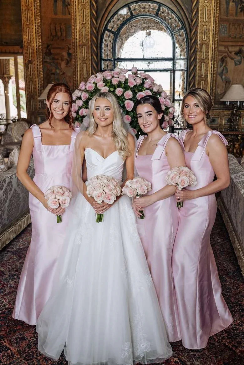 Model wearing a long pink satin bridesmaid dress with a square neckline, double straps, and decorative bows.