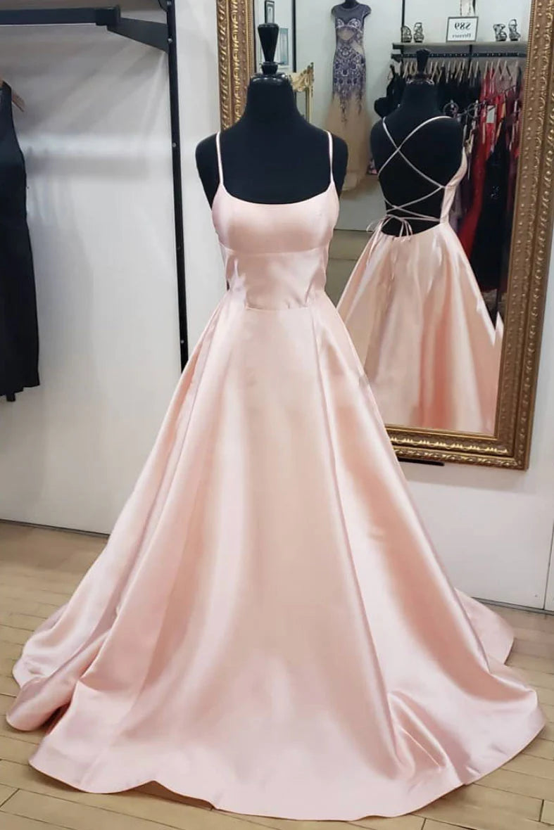 Woman wearing an elegant pink satin long prom dress with spaghetti straps and a backless design.