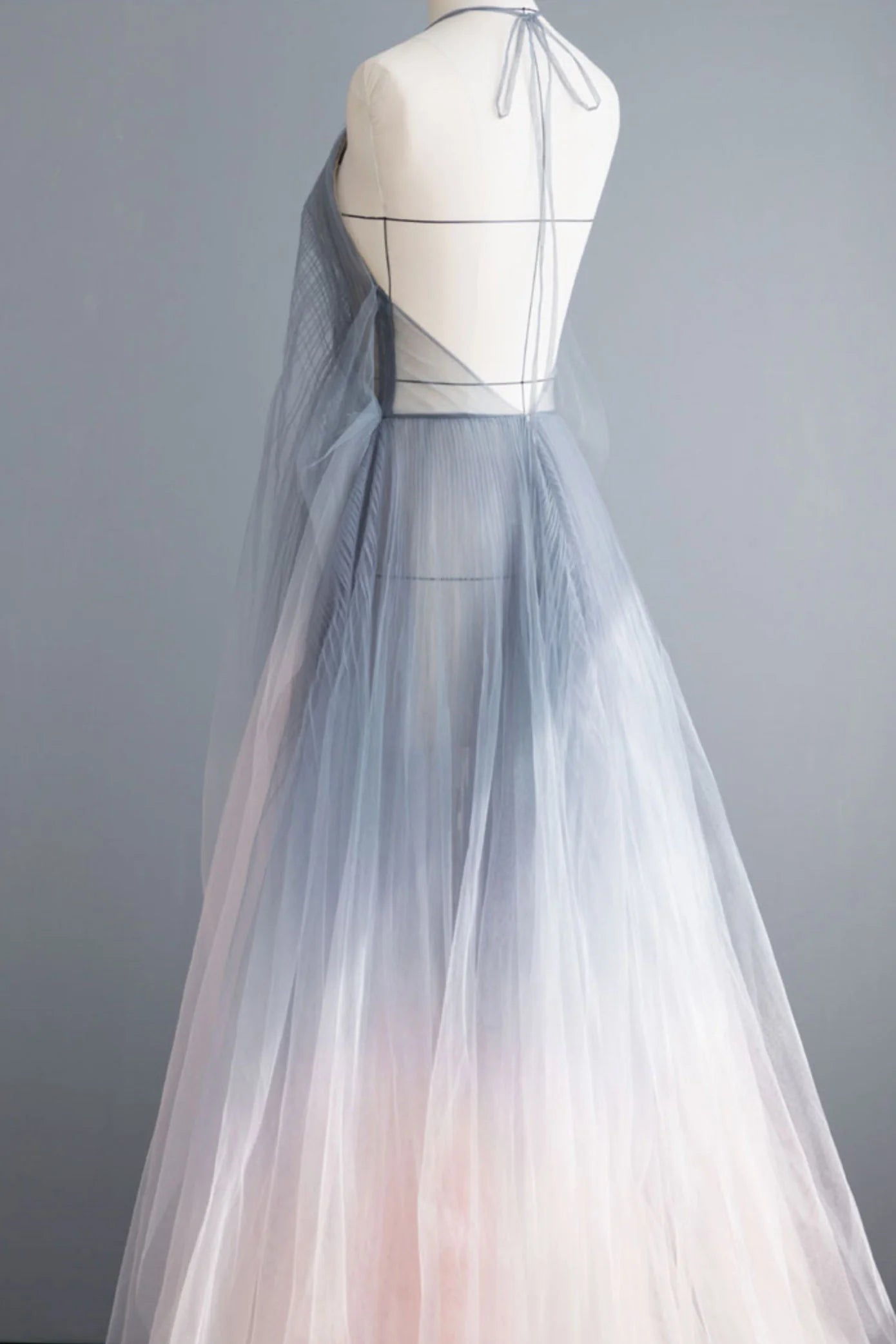 Side view of a woman wearing a flowing gray tulle long prom dress with spaghetti straps.