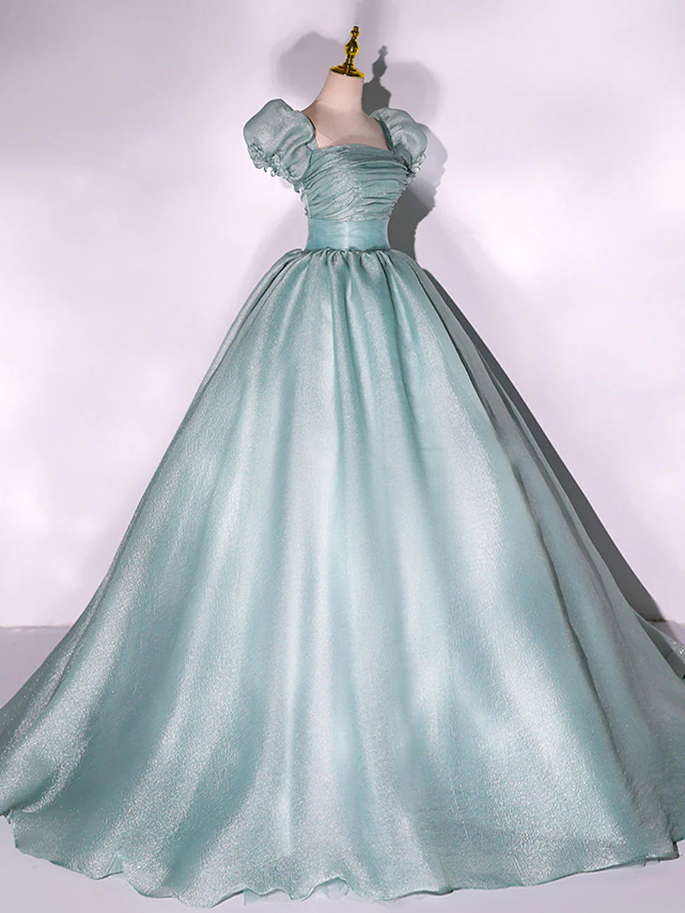 Side view of a long green formal gown with puff sleeves and flowing A-line skirt.