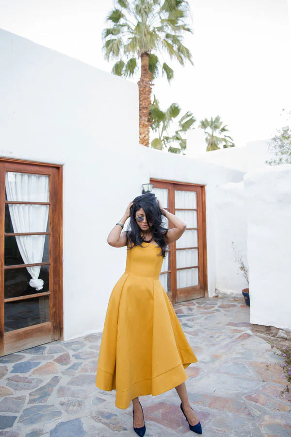 Model posing in a vibrant yellow off-shoulder short satin evening dress, side view.