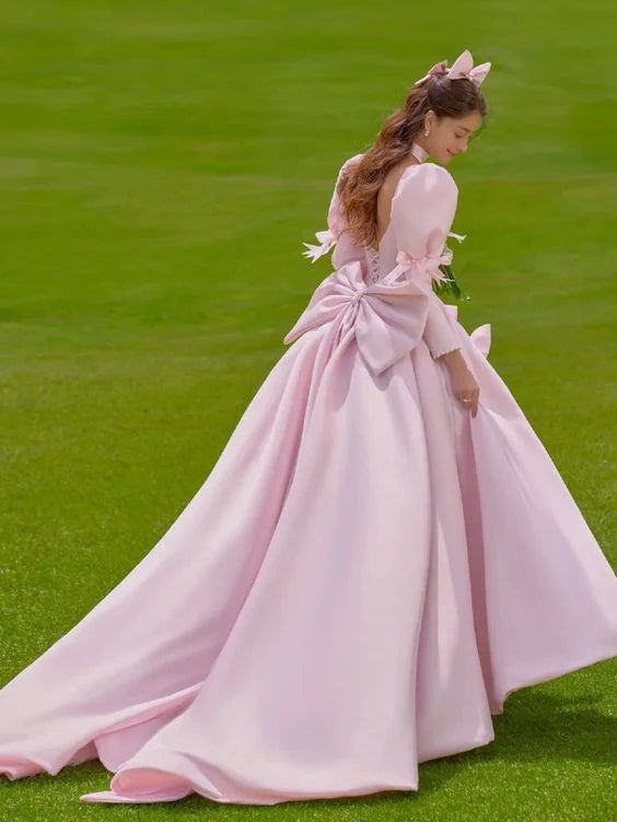 Side view of a woman in a flowing pink A-line long prom dress with puff sleeves.