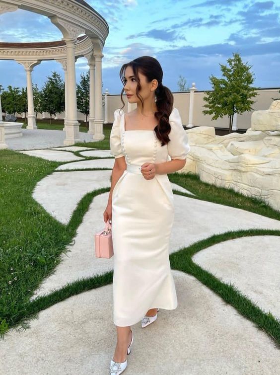 Elegant woman wearing an ivory satin short sleeve A-line evening dress, full length view.