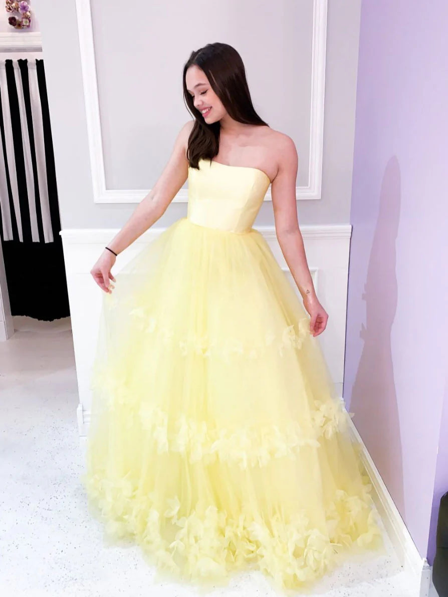 Model wearing a long yellow tulle prom dress with 3D floral appliques and intricate beading.