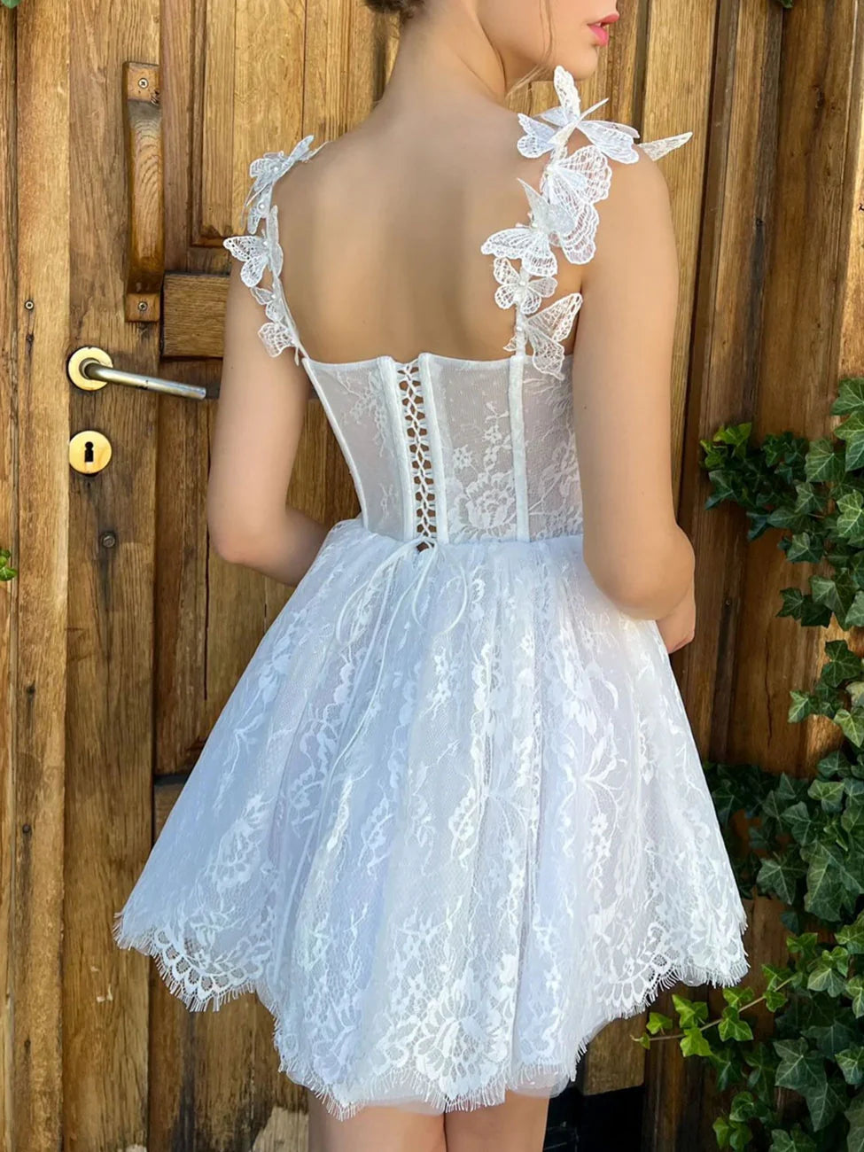 Model wearing an elegant white lace mini homecoming dress, side view.