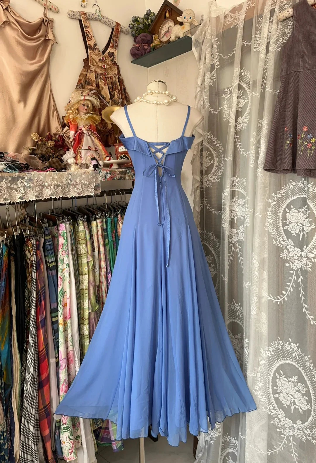 Model posing in a blue spaghetti strap evening gown, back view, highlighting the sophisticated design.