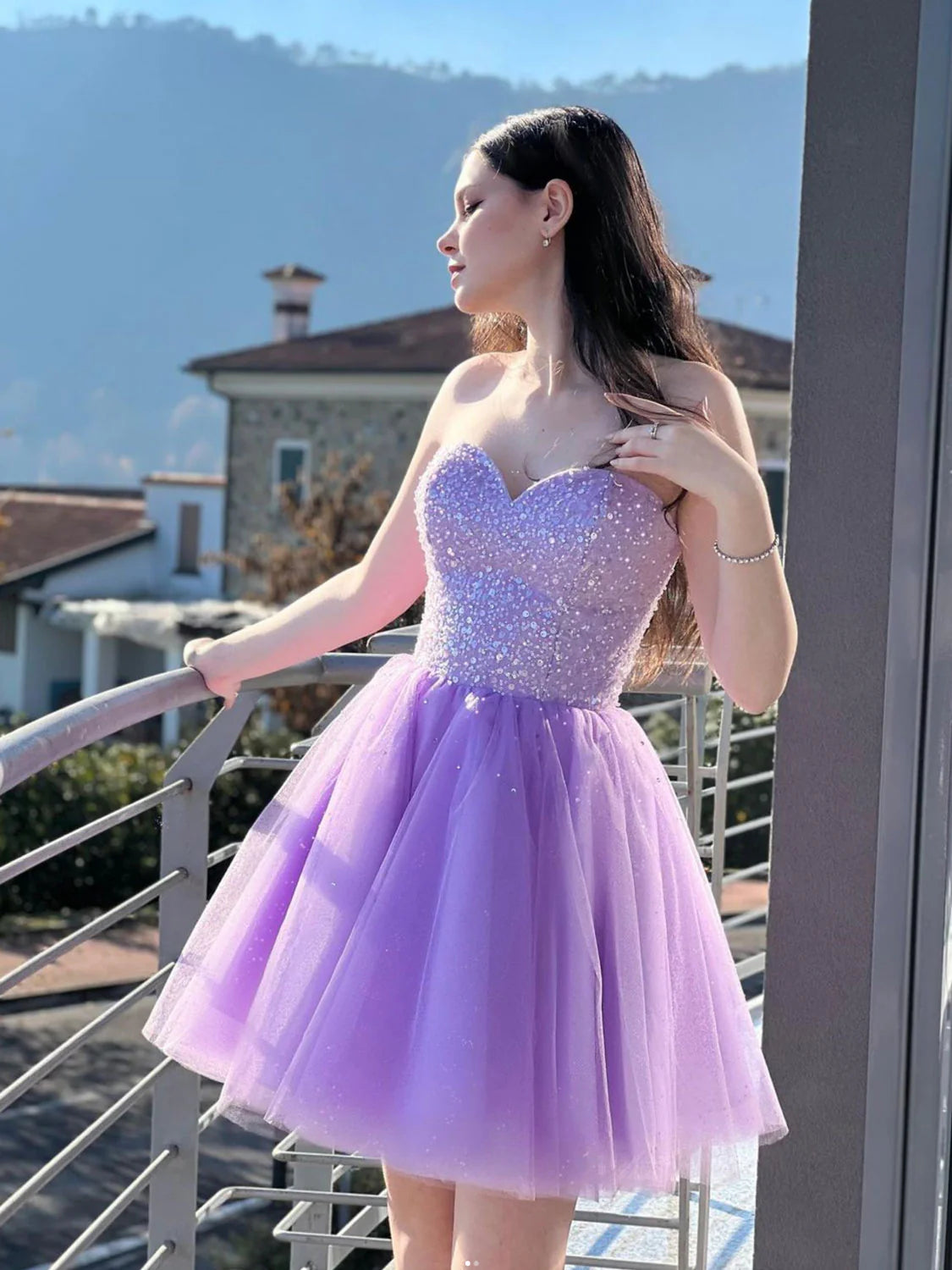 Model wearing a short purple sweetheart neck off-shoulder prom dress, posing elegantly.
