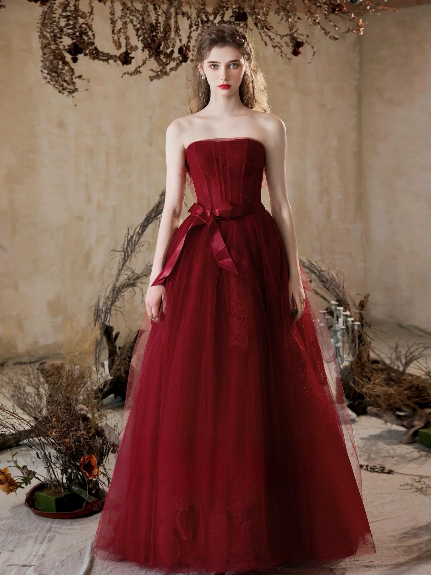 Woman wearing a long burgundy A-line prom dress with delicate lace details.