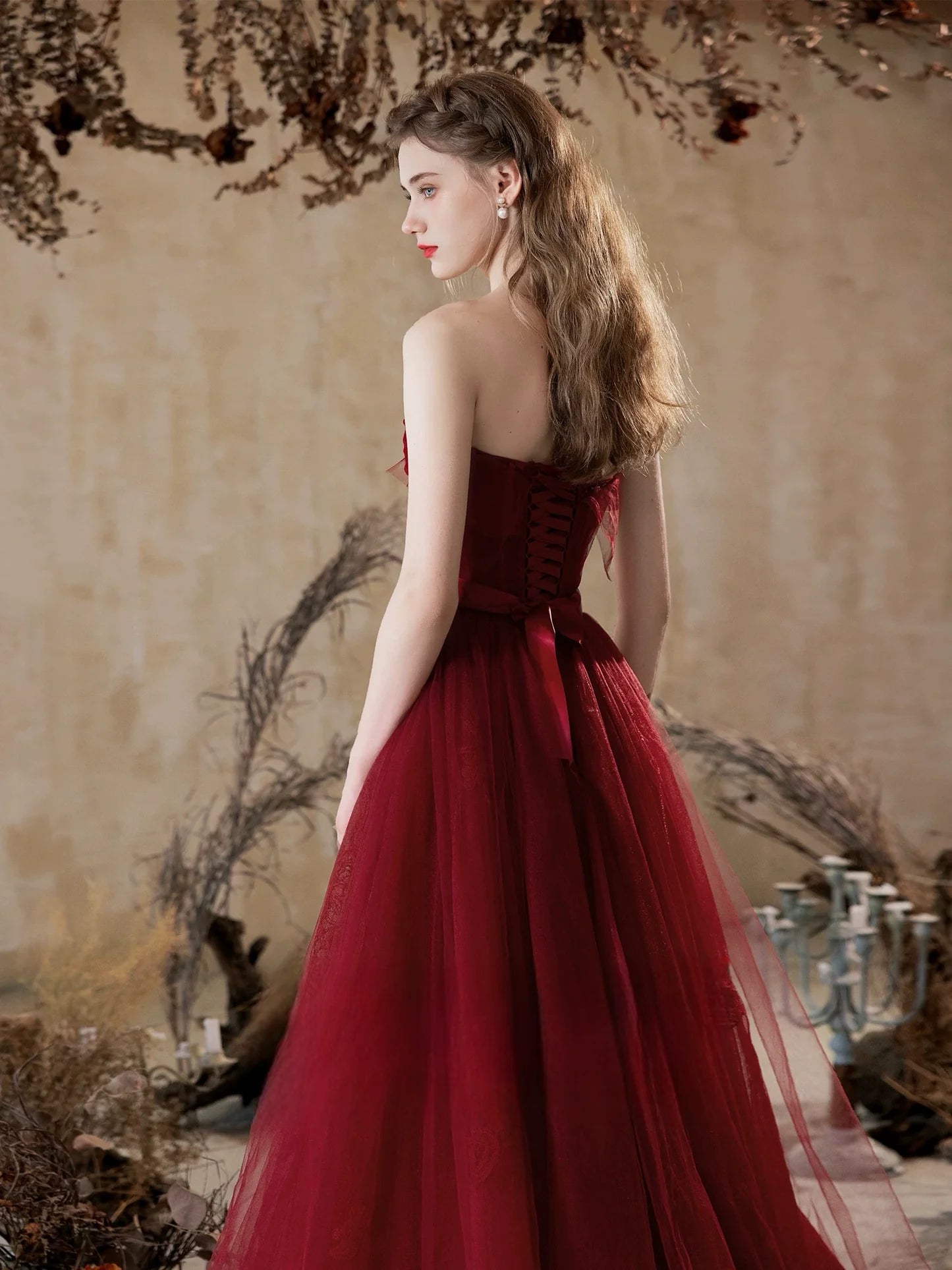 Side view of a woman in a flowing burgundy formal gown with tulle skirt.