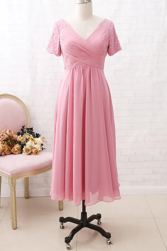 Full-length view of a woman in an elegant pink chiffon V-neck beaded sleeve mother of the bride dress.