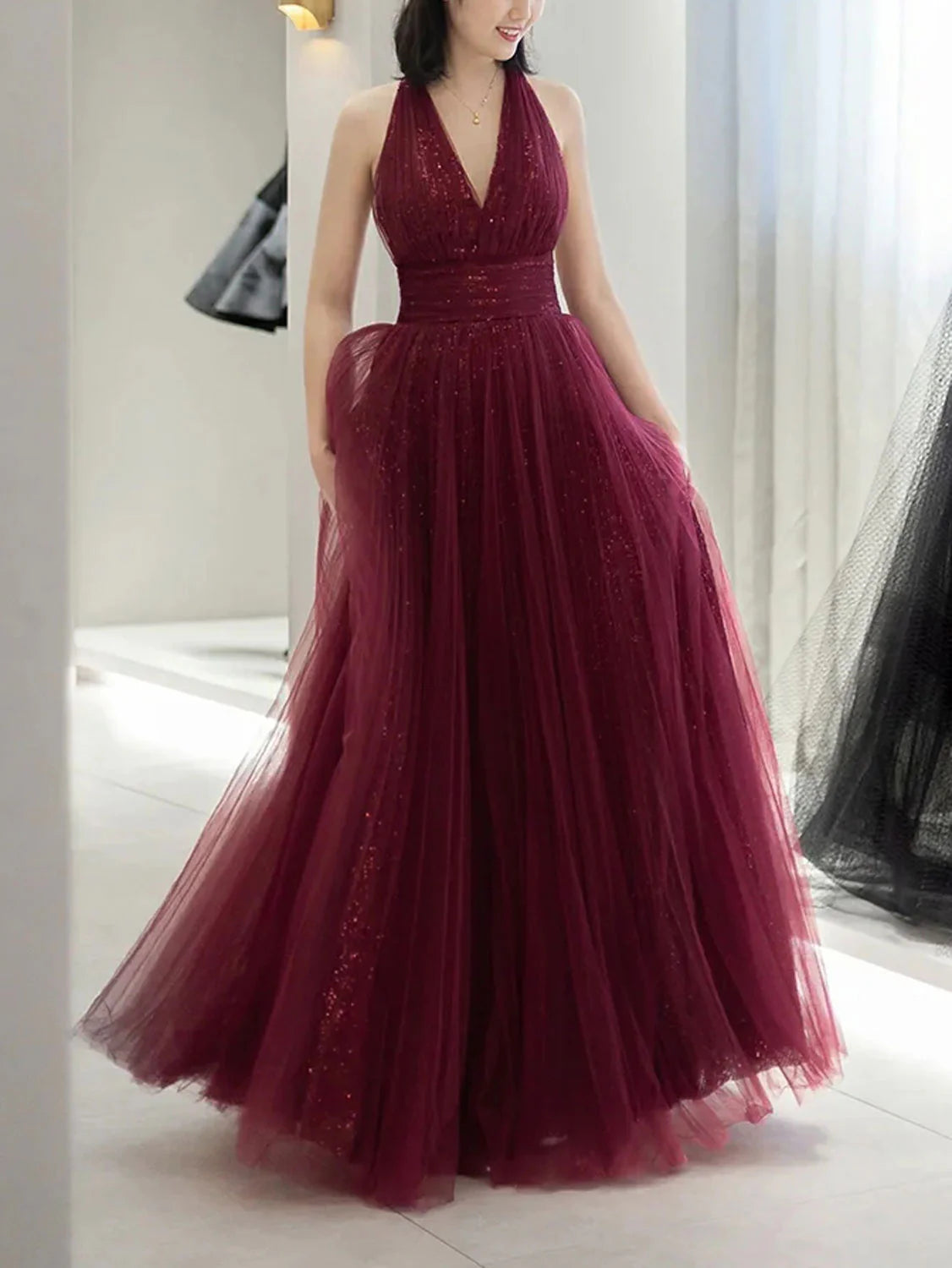 Model wearing a long burgundy A-line sequin prom dress with V-neck and halter straps.