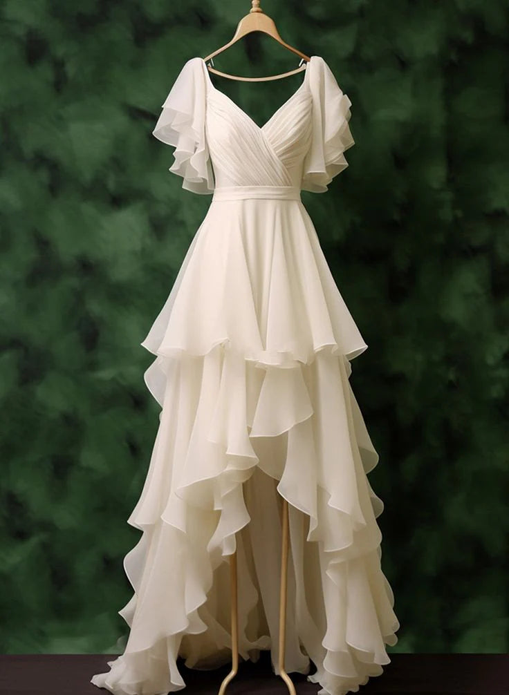 Model wearing an ivory chiffon V-neck A-line high-low wedding dress with ruffled short sleeves.