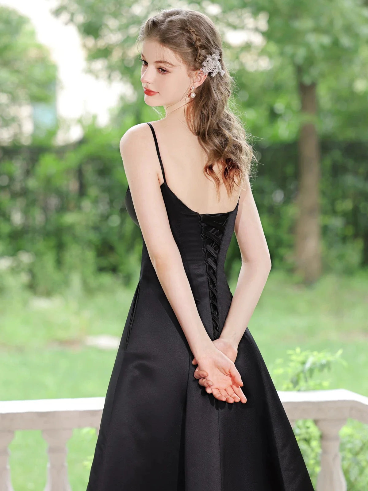 Woman in elegant black A-line V-neck tea-length satin prom dress, side view.