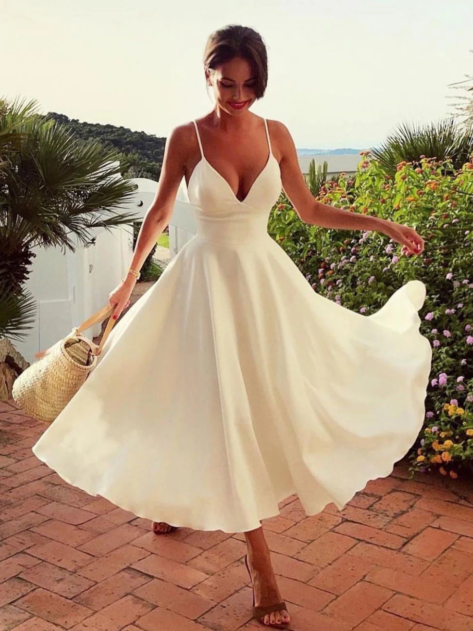 Woman in elegant white A-line V-neck satin tea-length dress, side view.