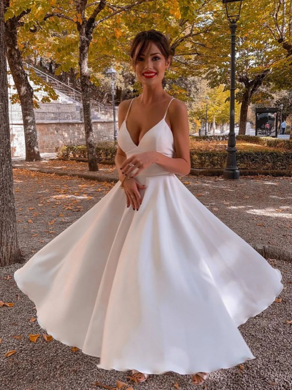 Woman in elegant white A-line V-neck satin tea-length dress, front view.