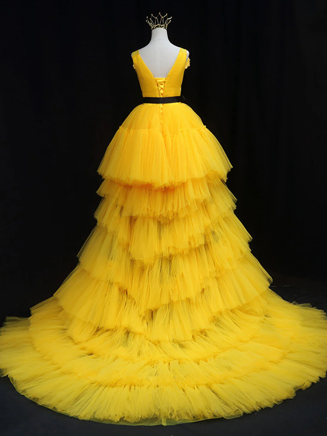 Back view of a woman wearing a vibrant yellow tulle floor-length gown, highlighting the elegant drape.
