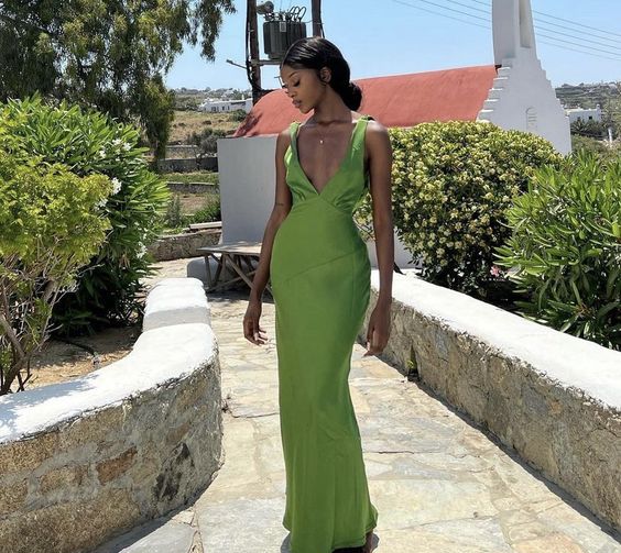 Woman wearing an elegant green satin V-neck sleeveless prom dress with a high slit.