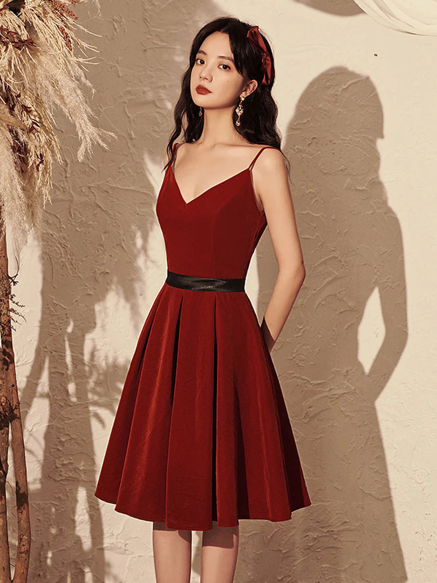 Model wearing a burgundy velvet V-neck short prom dress with spaghetti straps.