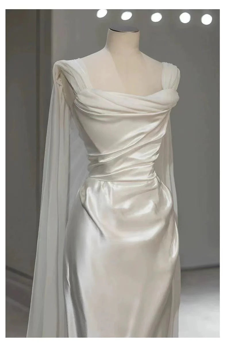 Side view of a bride in a white satin pleated A-line wedding gown with a flowing skirt.