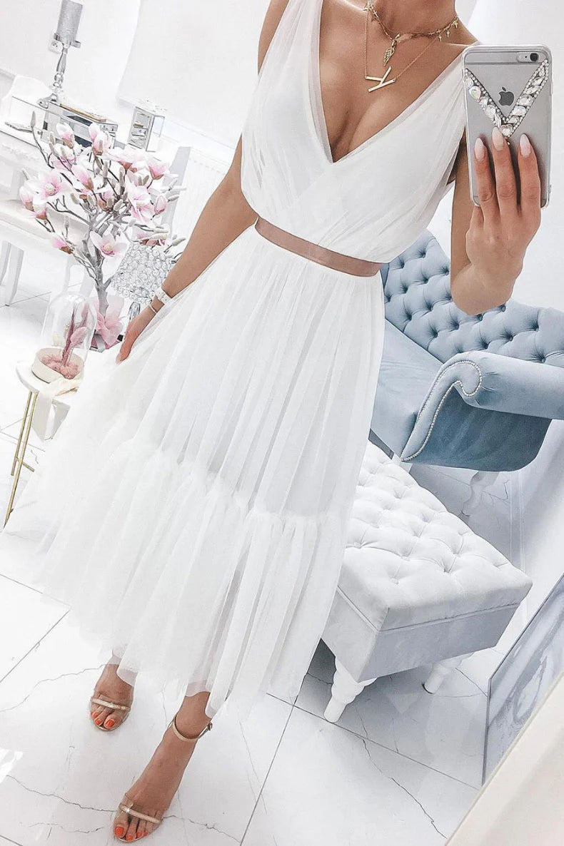 A woman posing in a flowing white V-neck formal gown with chiffon and tulle details.