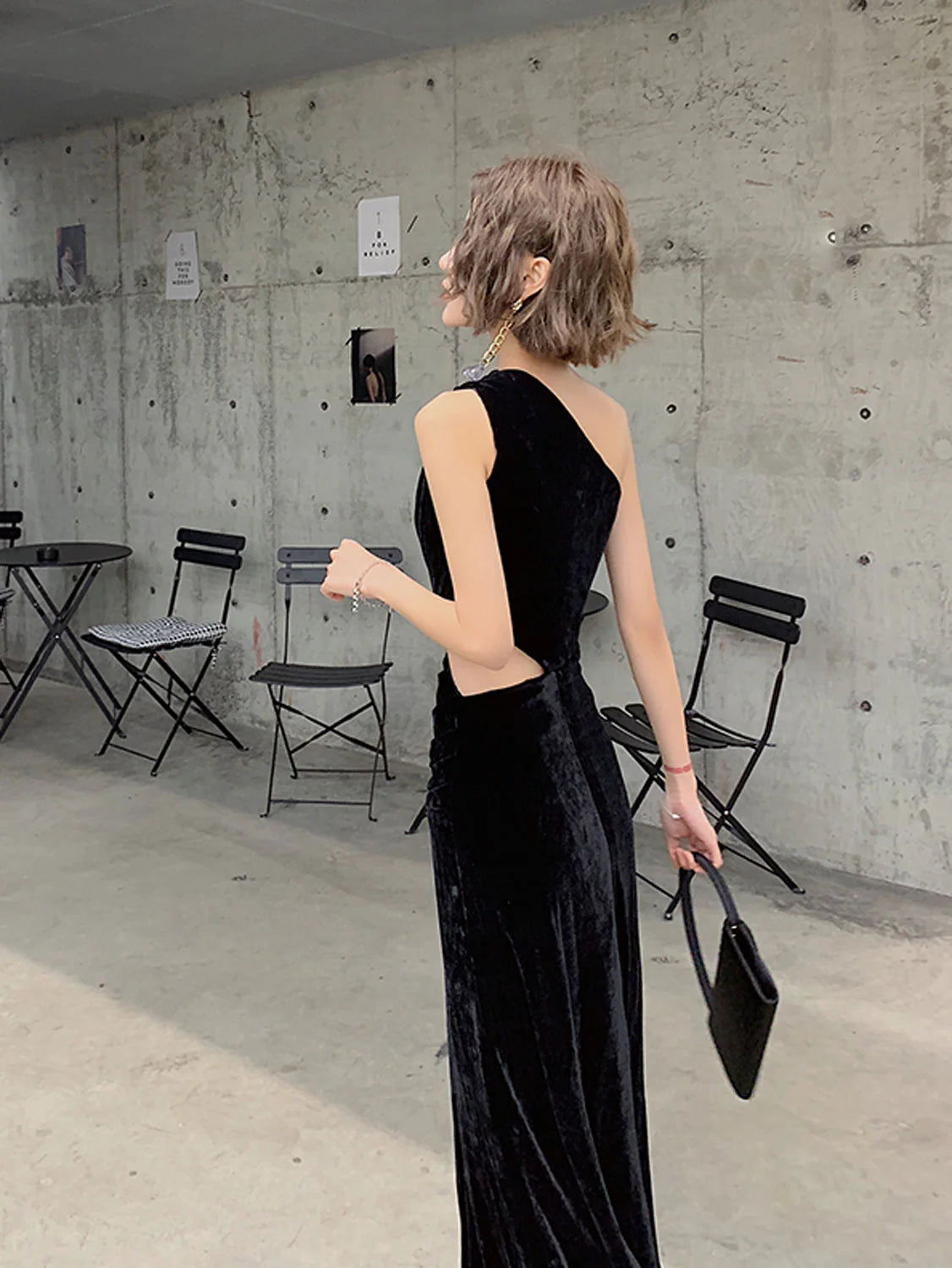 Side view of a model wearing a black velvet one-shoulder evening gown.