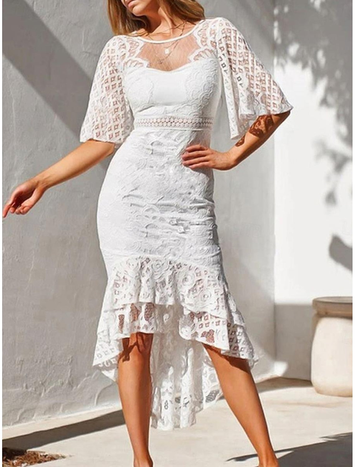 Woman posing elegantly in a white lace ruffle asymmetrical midi dress.