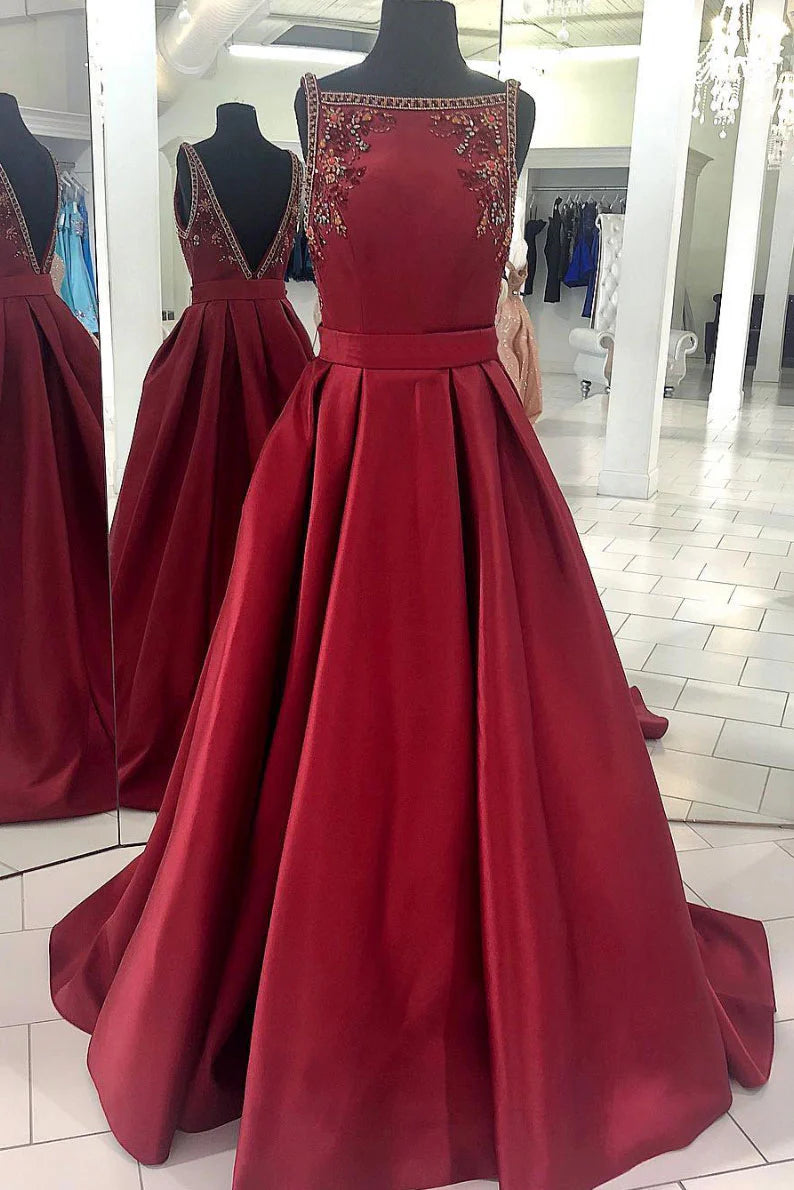 Woman wearing a long burgundy satin backless prom dress with beaded straps.