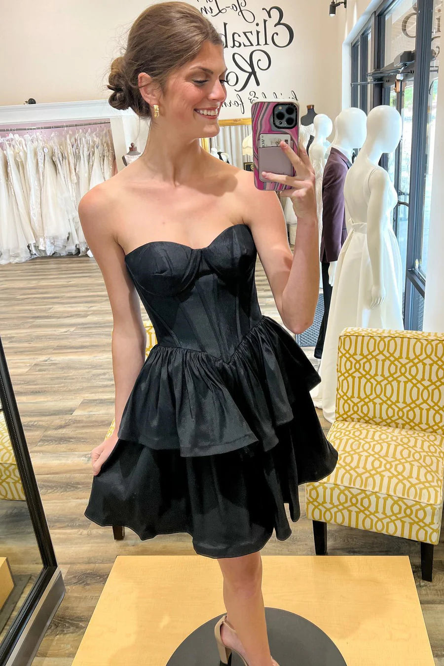 Woman wearing a black strapless A-line short party dress with sweetheart neckline.