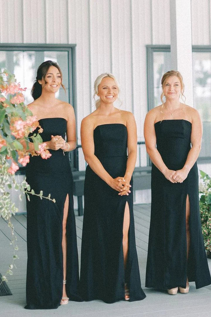 Model wearing an elegant black strapless mermaid satin bridesmaid dress with a high slit.