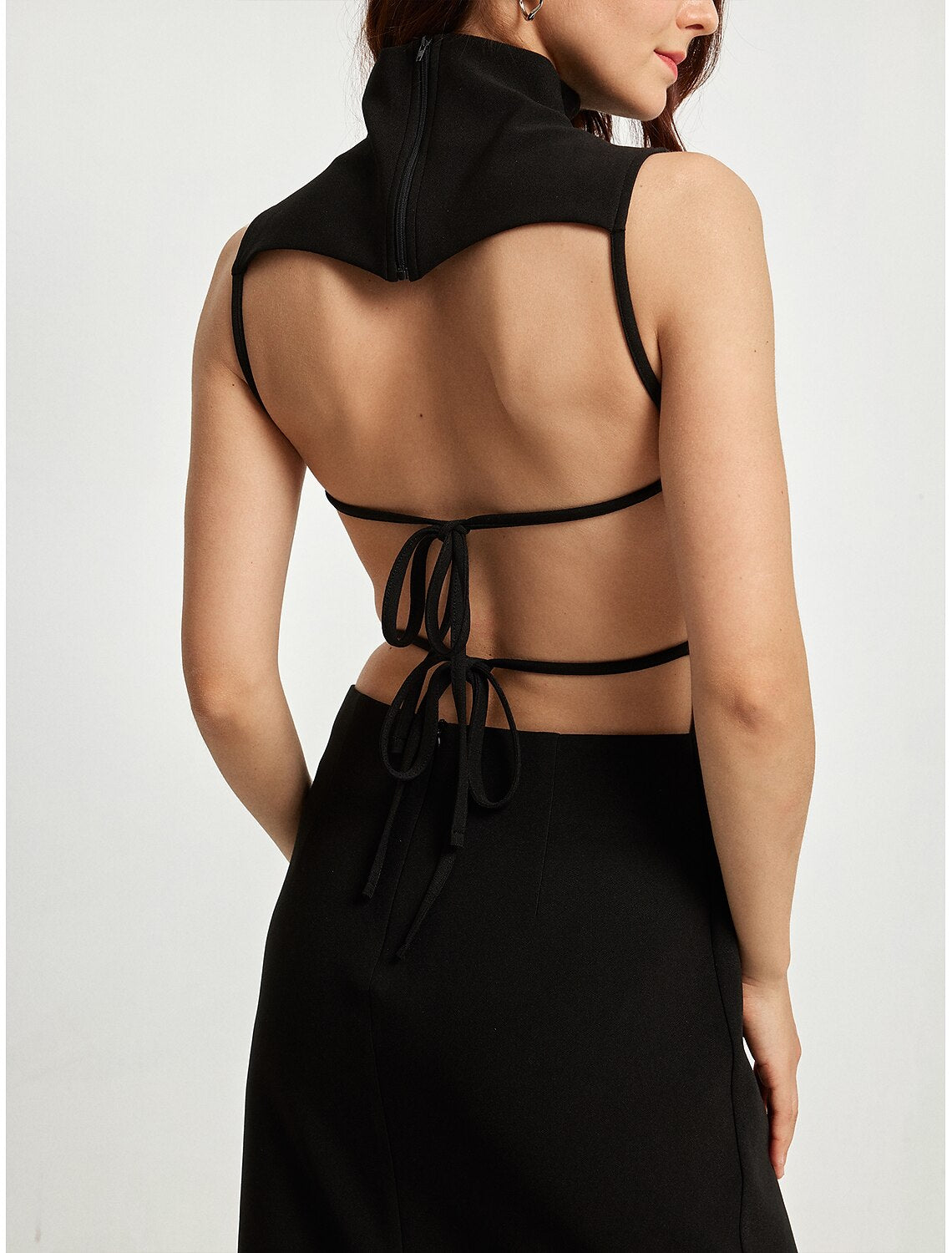 Woman modeling an elegant black high neck sleeveless midi dress with a high slit, side view.