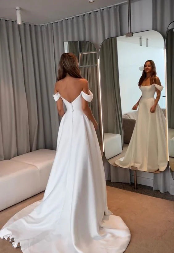 Woman in elegant white satin A-line off-shoulder wedding dress with long train and slit.