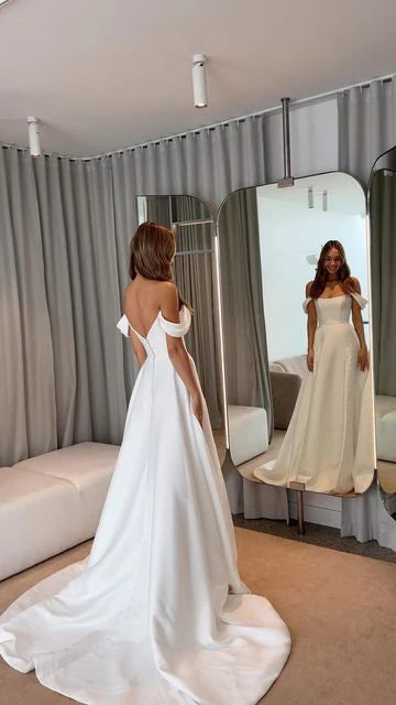 Close-up of white satin A-line off-shoulder wedding dress fabric and design details.