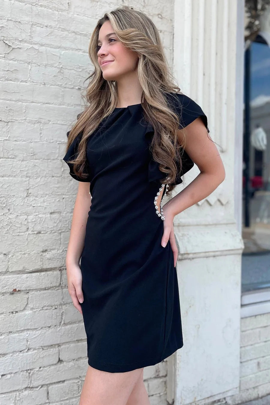 Model wearing a black cutout short party dress with ruffled sleeves and pearl details.
