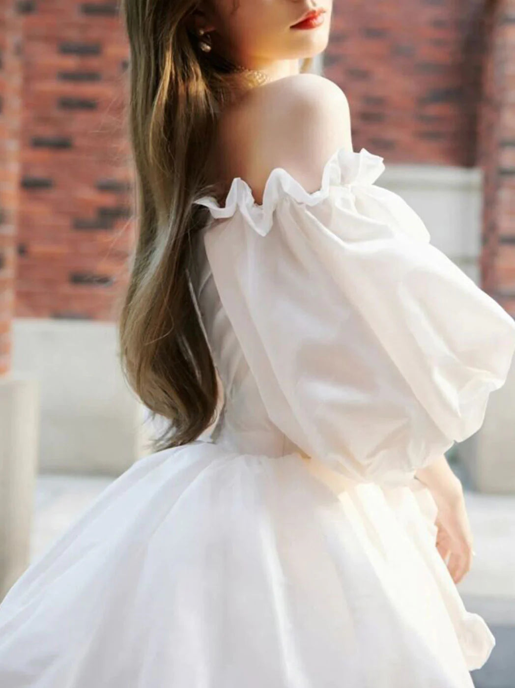 Side view of a woman wearing a white long sleeve A-line short evening dress.