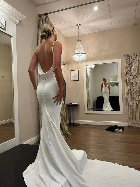 Woman wearing an elegant white mermaid wedding dress with V-neck, spaghetti straps, and backless detail.