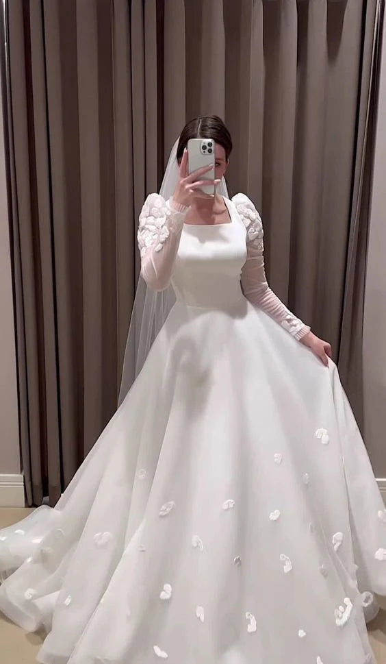 Full-length view of a woman in a white A-line wedding dress with long tulle sleeves.