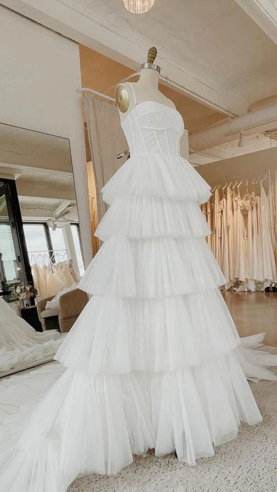 Model wearing an elegant white multi-layer mesh wedding dress with suspender straps and fishbone bodice.