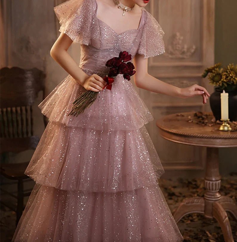 Back view of a pink waist-cinching multilayer floor-length evening dress, highlighting the flowing skirt.