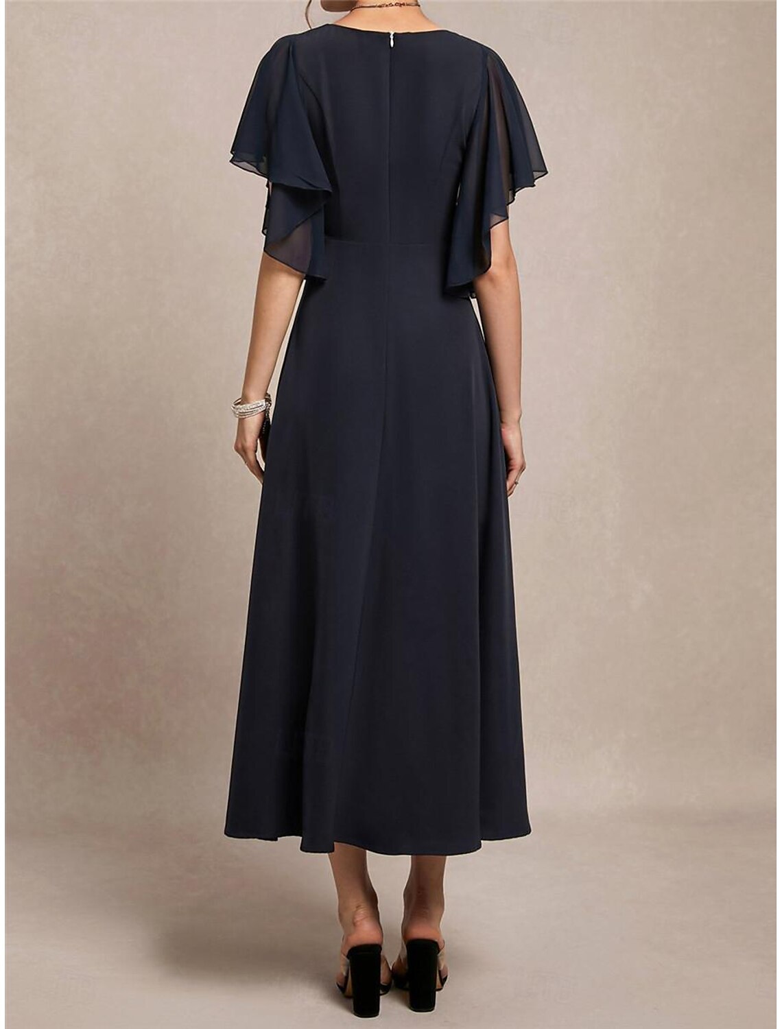 Side view of a woman in a navy blue A-line maxi dress, showing ruffle details and high waist.