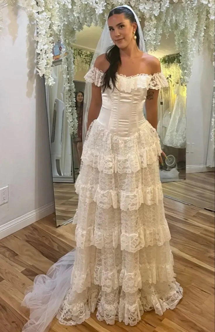 Elegant off-shoulder A-line lace wedding dress with a long layered skirt.